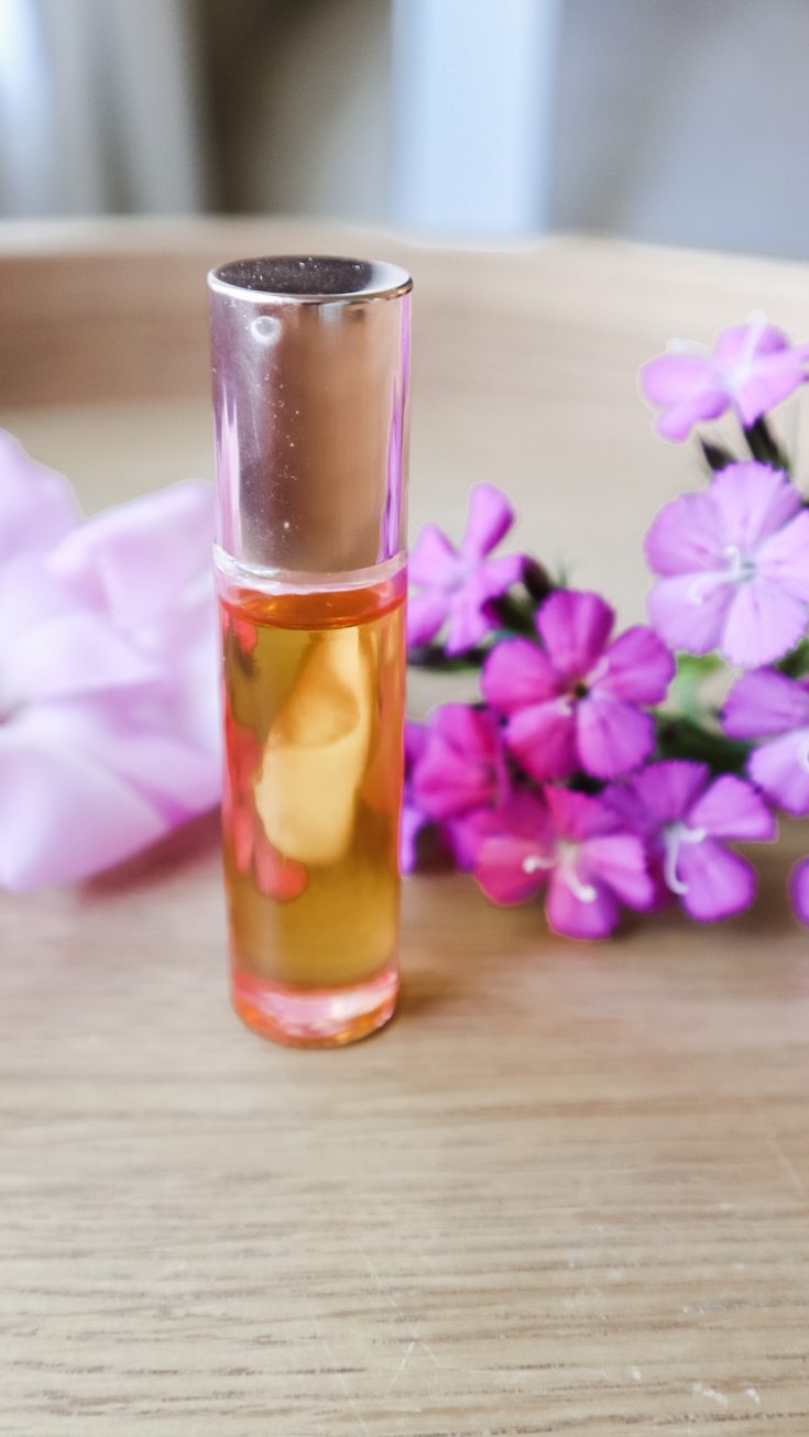 A bottle of DIY Cuticle Oil sitting on a table next to some purple flowers