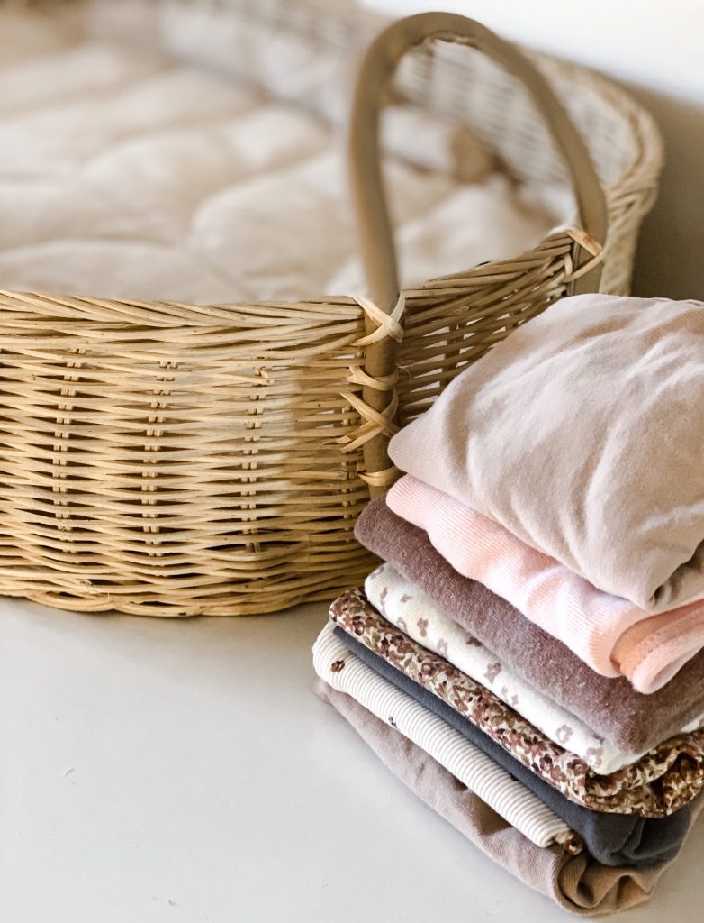 Folded baby clothes next to a baby changing basket