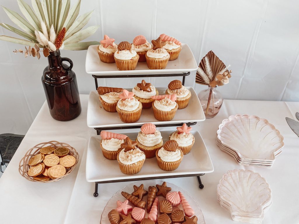 Cupcakes topped with seashell shaped chocolates sitting on a white table 