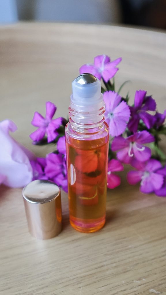 A roller bottle of DIY cuticle oil sitting on a table with flowers